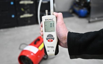 A hand holds a Bromic gas detector displaying 