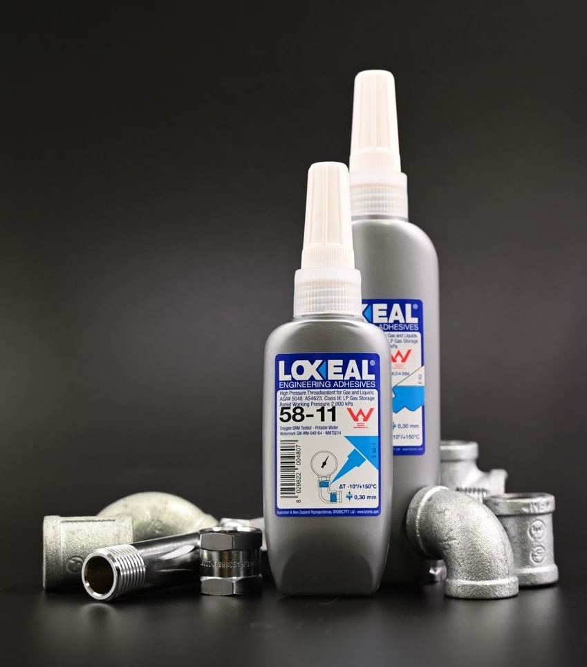 Bottles of Loxeal engineering adhesives stand upright among metal plumbing fittings on a black surface. The label on the front bottle reads: 