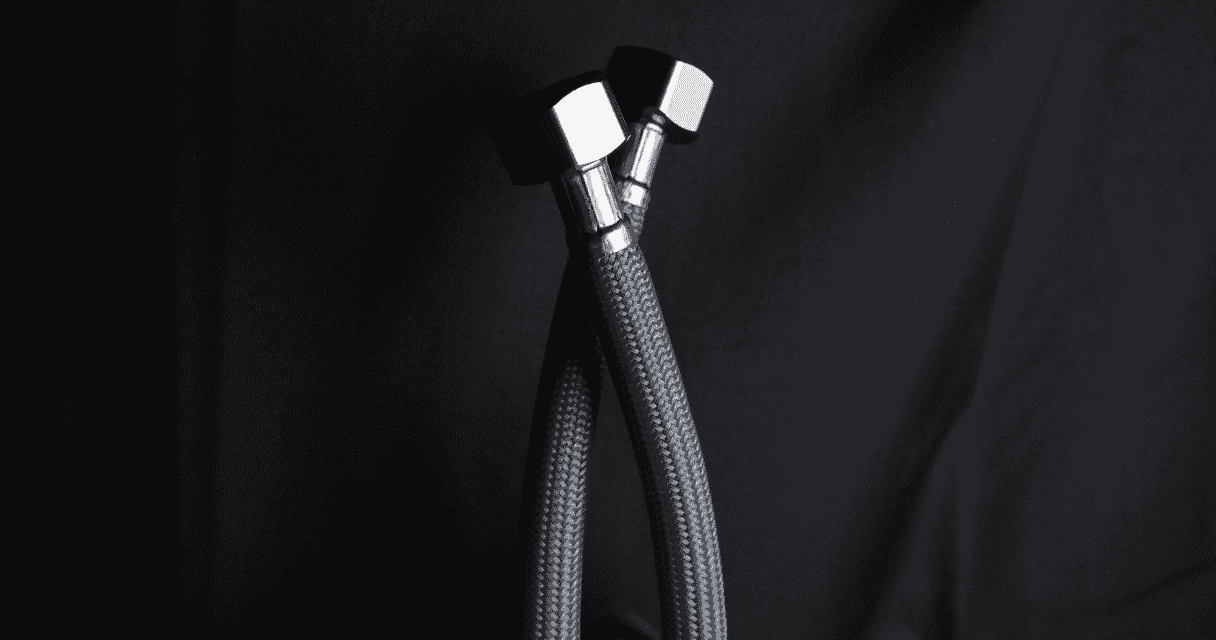 Close-up of two braided hoses ending in shiny metal hex fittings, set against a dark background